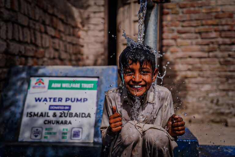 Smiling child playing at donor funded water pump