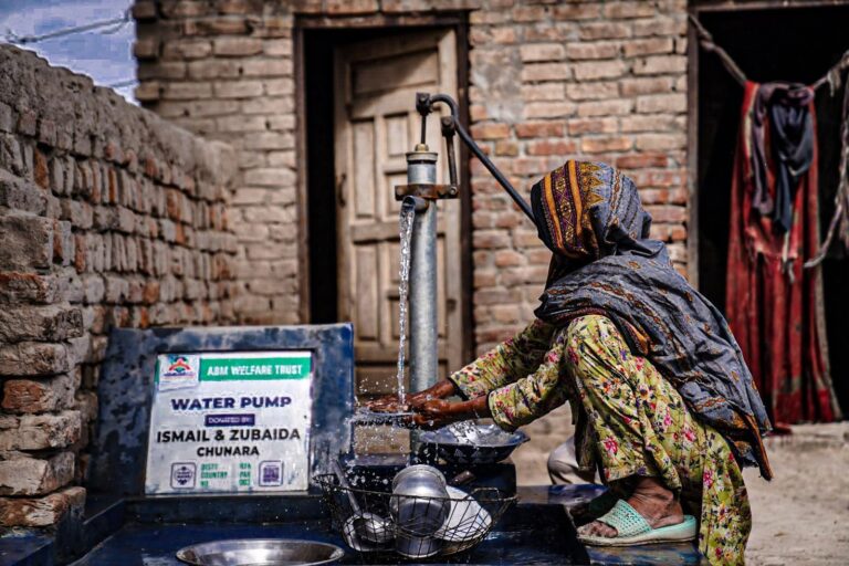 Woman washing dishes at clean water hand pump